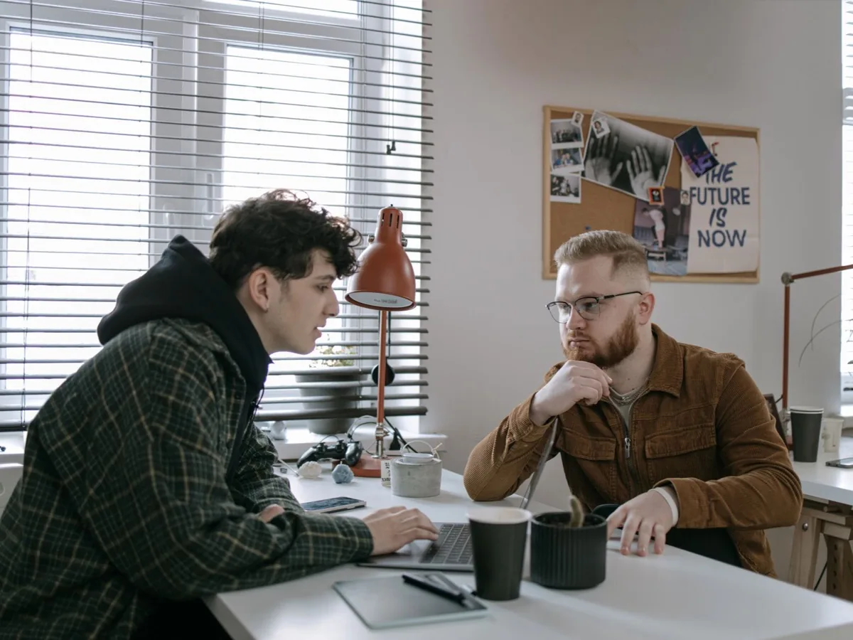 Twee mensen zitten tegenover elkaar aan een tafel bij het raam te werken.