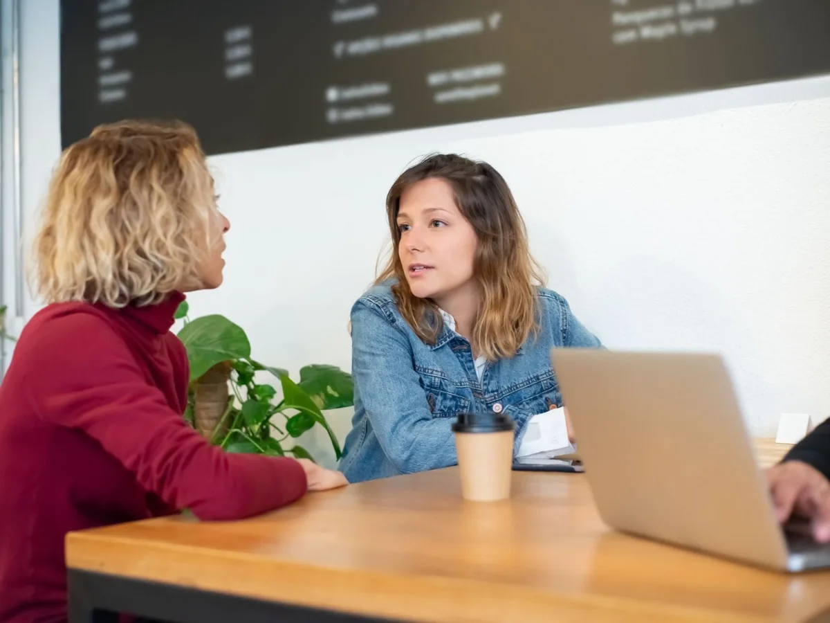Twee vrouwen kijken samen naar een laptop aan een tafel.