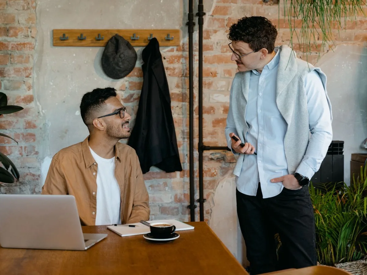 Twee mensen kijken samen naar een laptop aan een houten tafel.