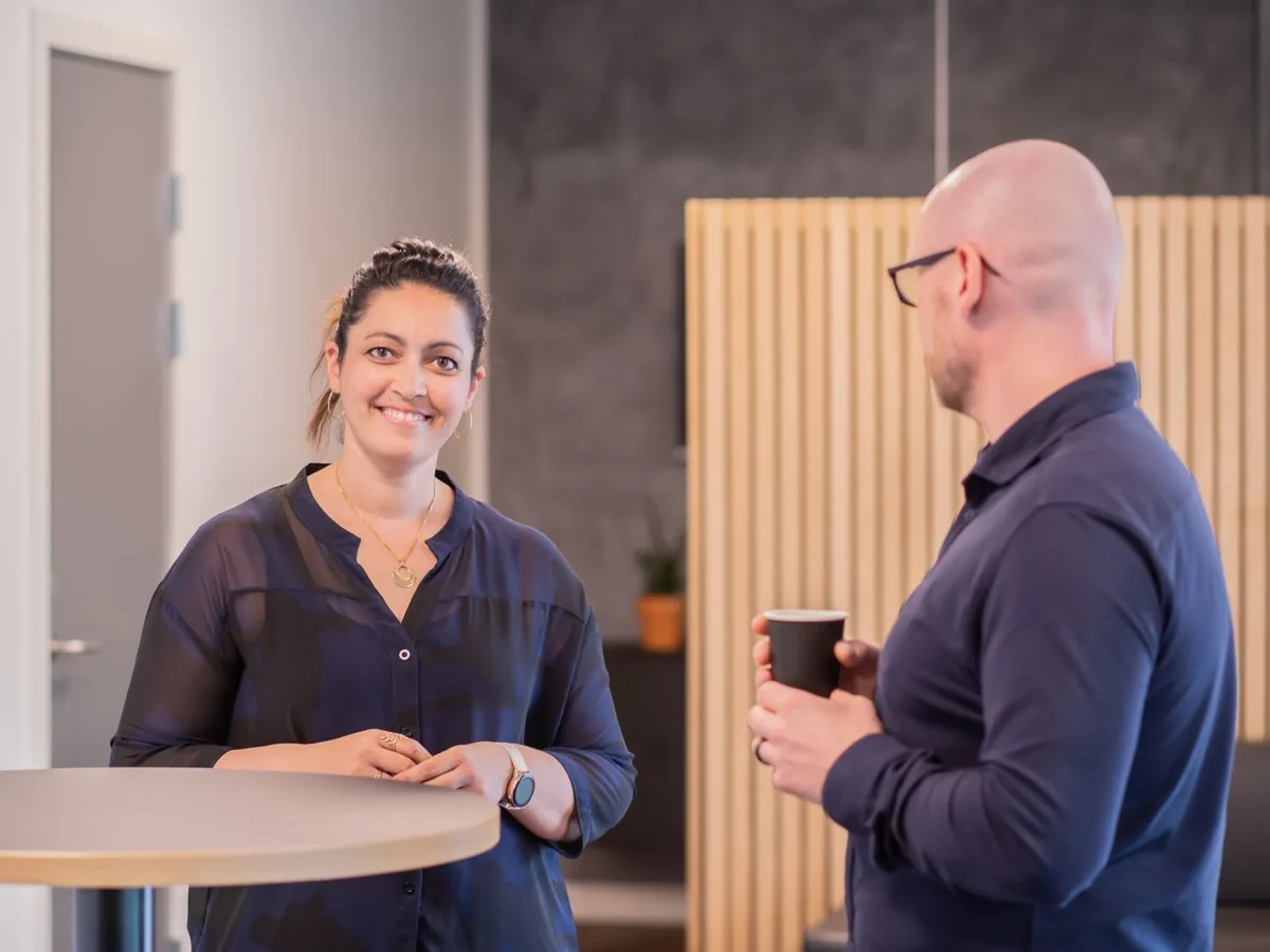 Twee collega's staan met een kop koffie te overleggen in een kantoor.