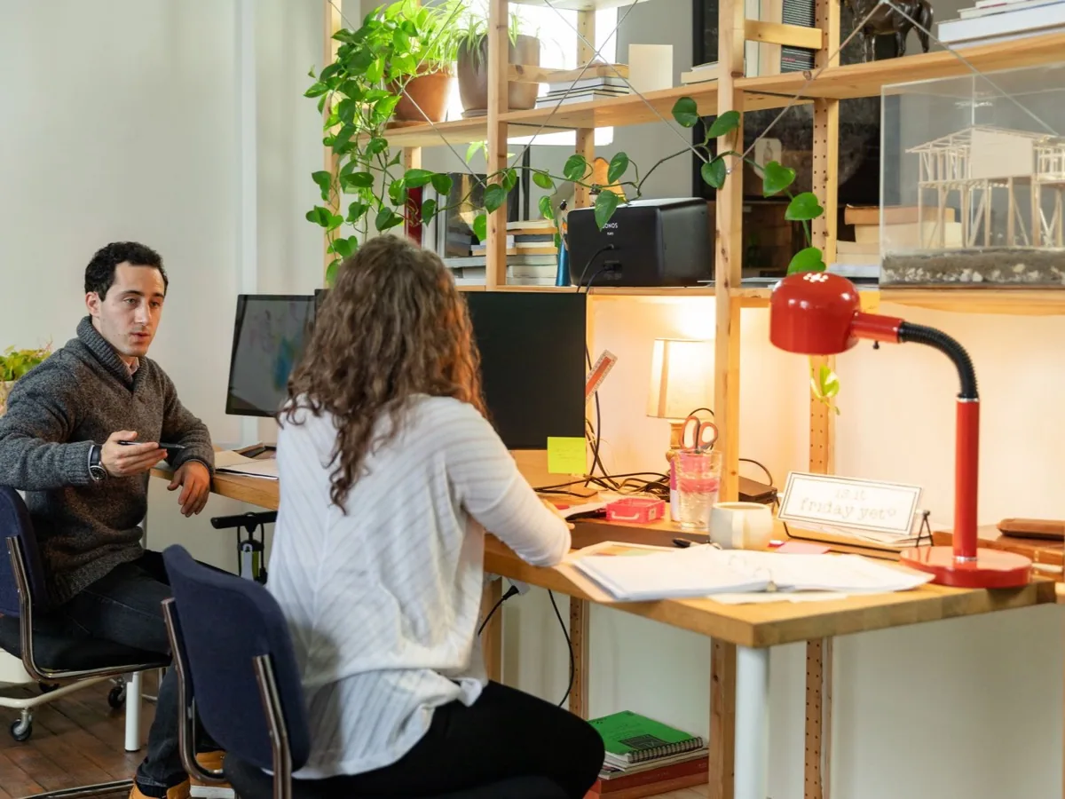 Twee mensen werken aan naastgelegen bureaus onder een bureaulamp.